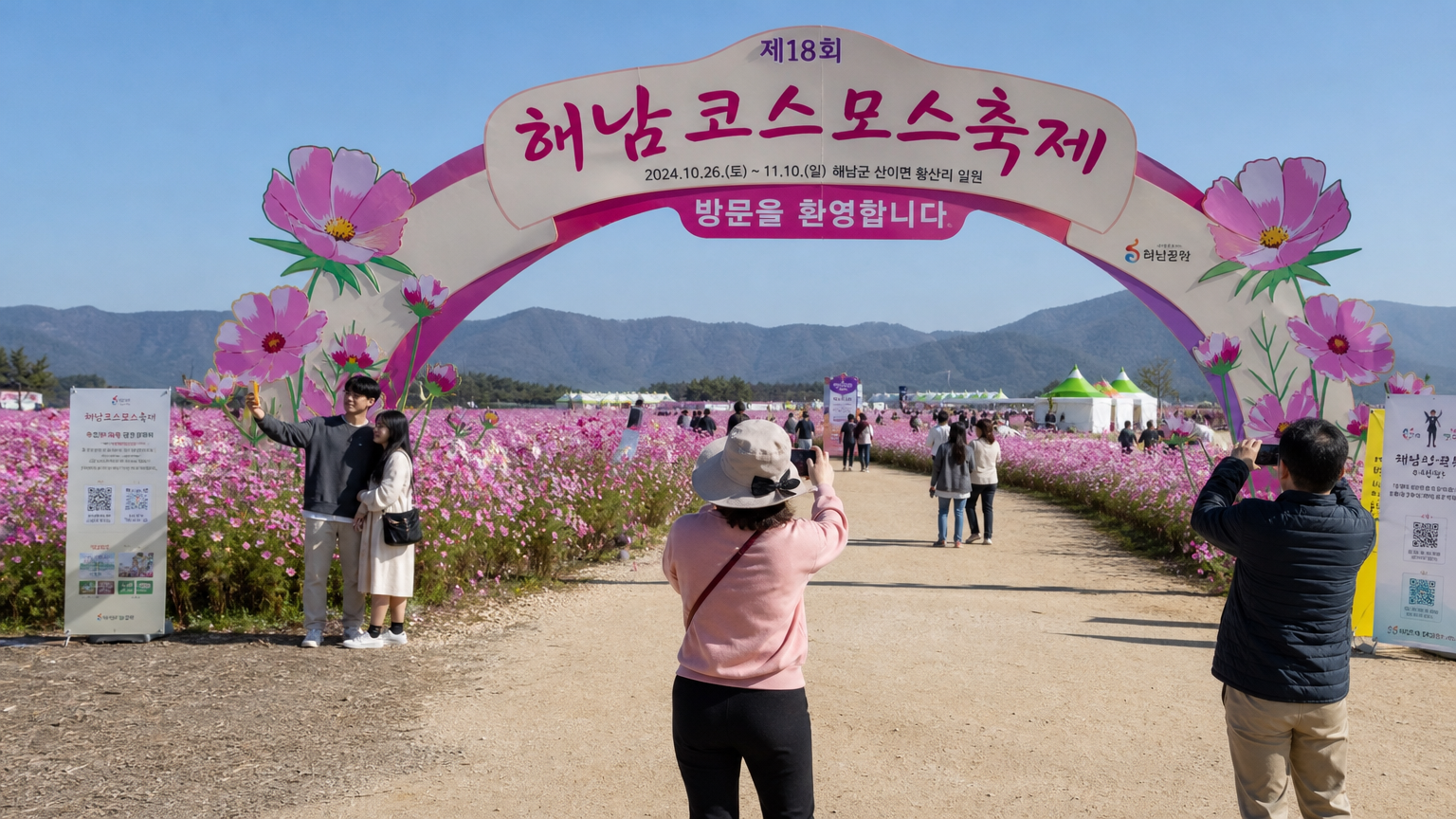 대형 환영 아치와 광활한 분홍빛 코스모스로 꾸며진 행사장 입구에서 사진 찍는 사람들