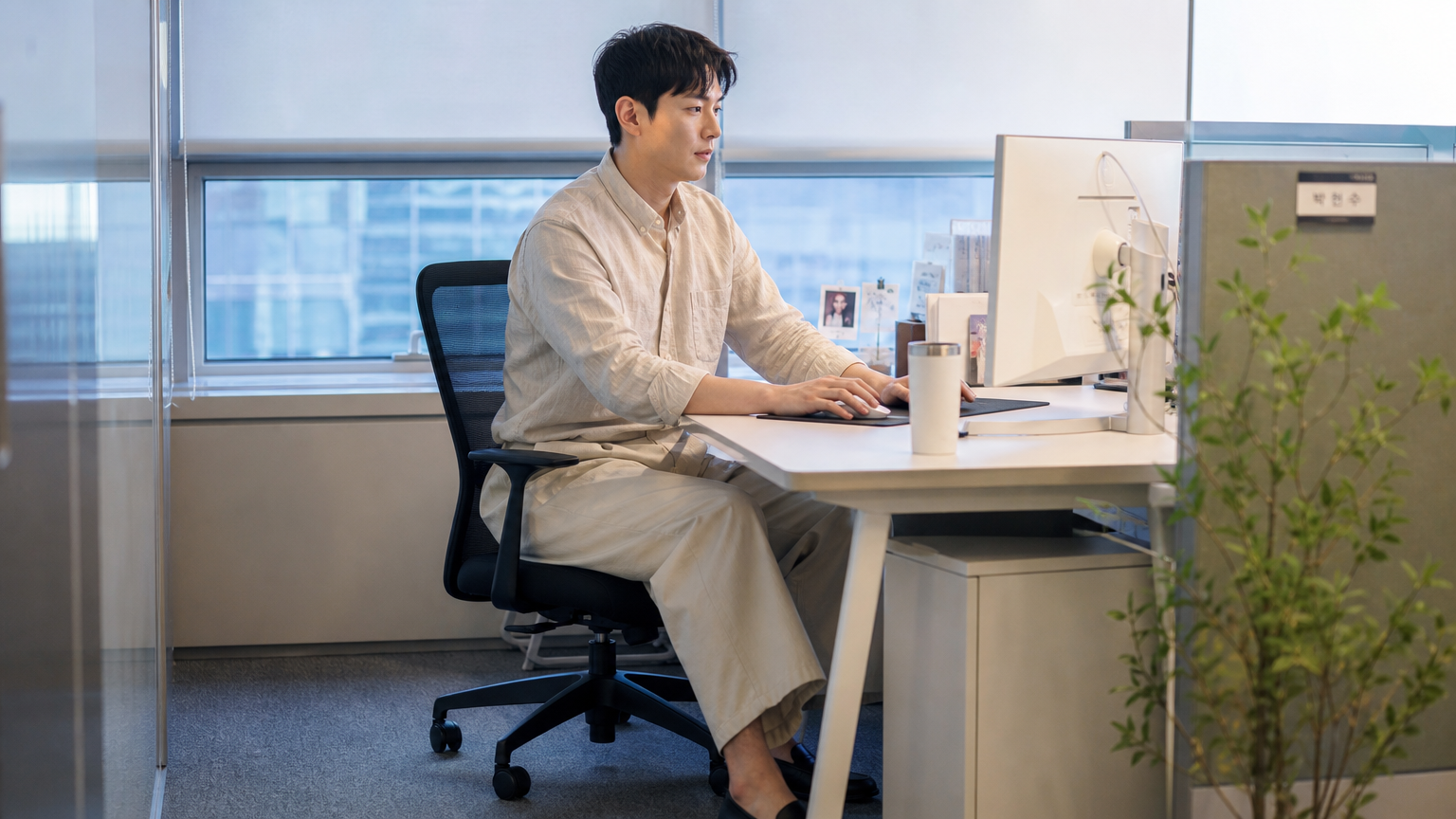 와이드 레그 팬츠와 린넨 셔츠를 입고 사무실 책상에 앉아 있는 사람