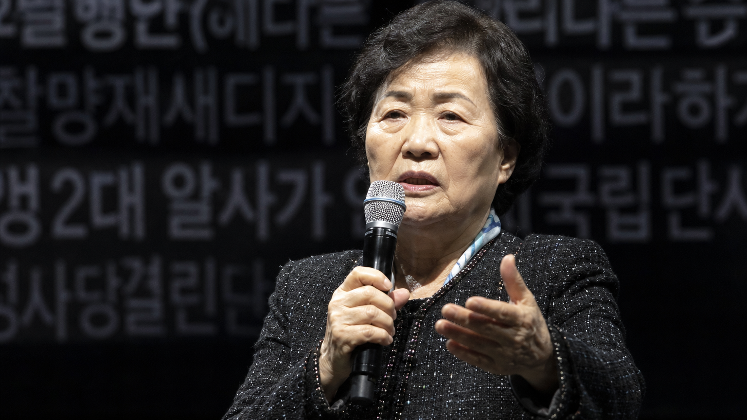 무대 위에서 마이크를 들고 관객에게 심각하게 발언하는 노년 여성 가수