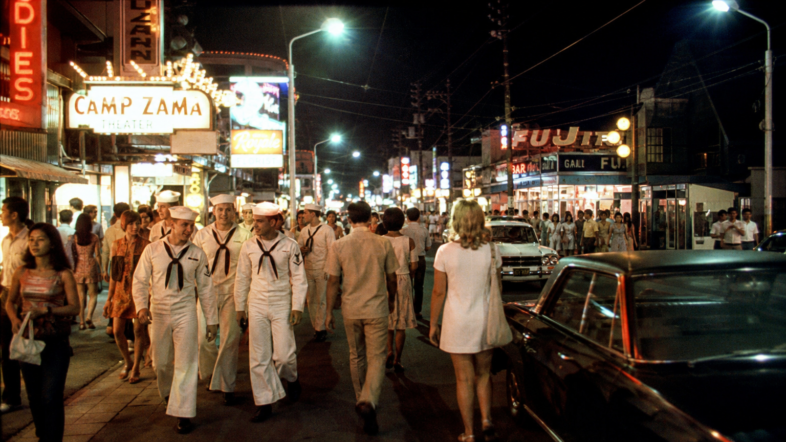 1970년대 미국 군사 기지 근처에서 젊은이들의 문화와 네온 불빛으로 번화한 거리 풍경