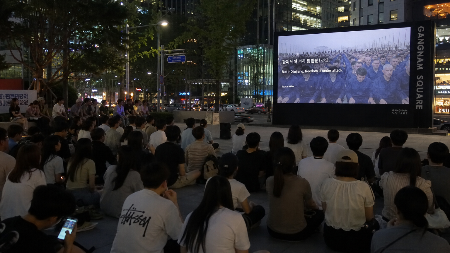 한국의 젊은 성인들이 야외 광장에서 신장 위구르 관련 다큐멘터리를 시청하는 장면
