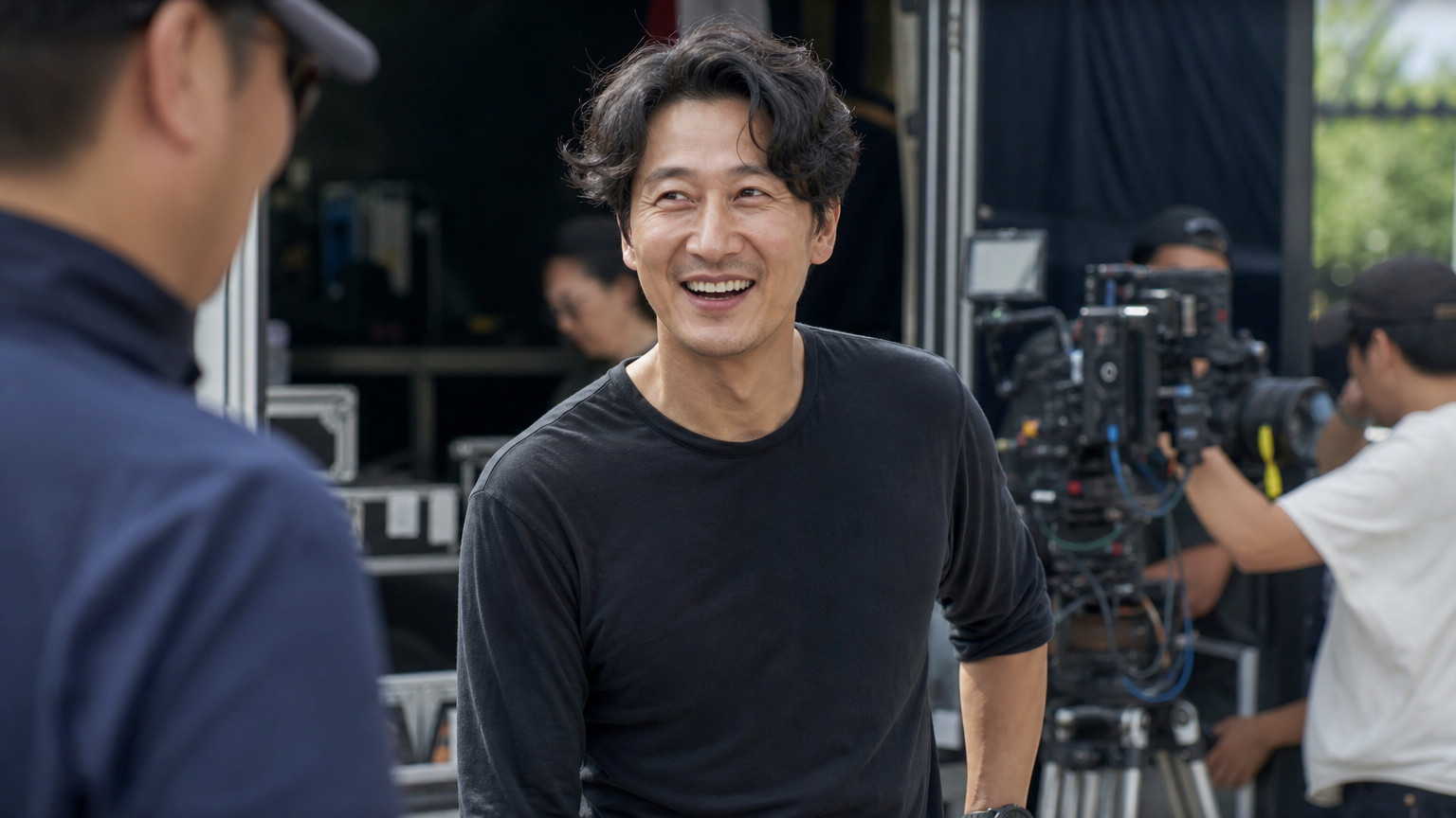 편안한 옷차림의 카리스마 있는 중년 배우가 촬영장에서 유머러스한 분위기를 연출하는 모습