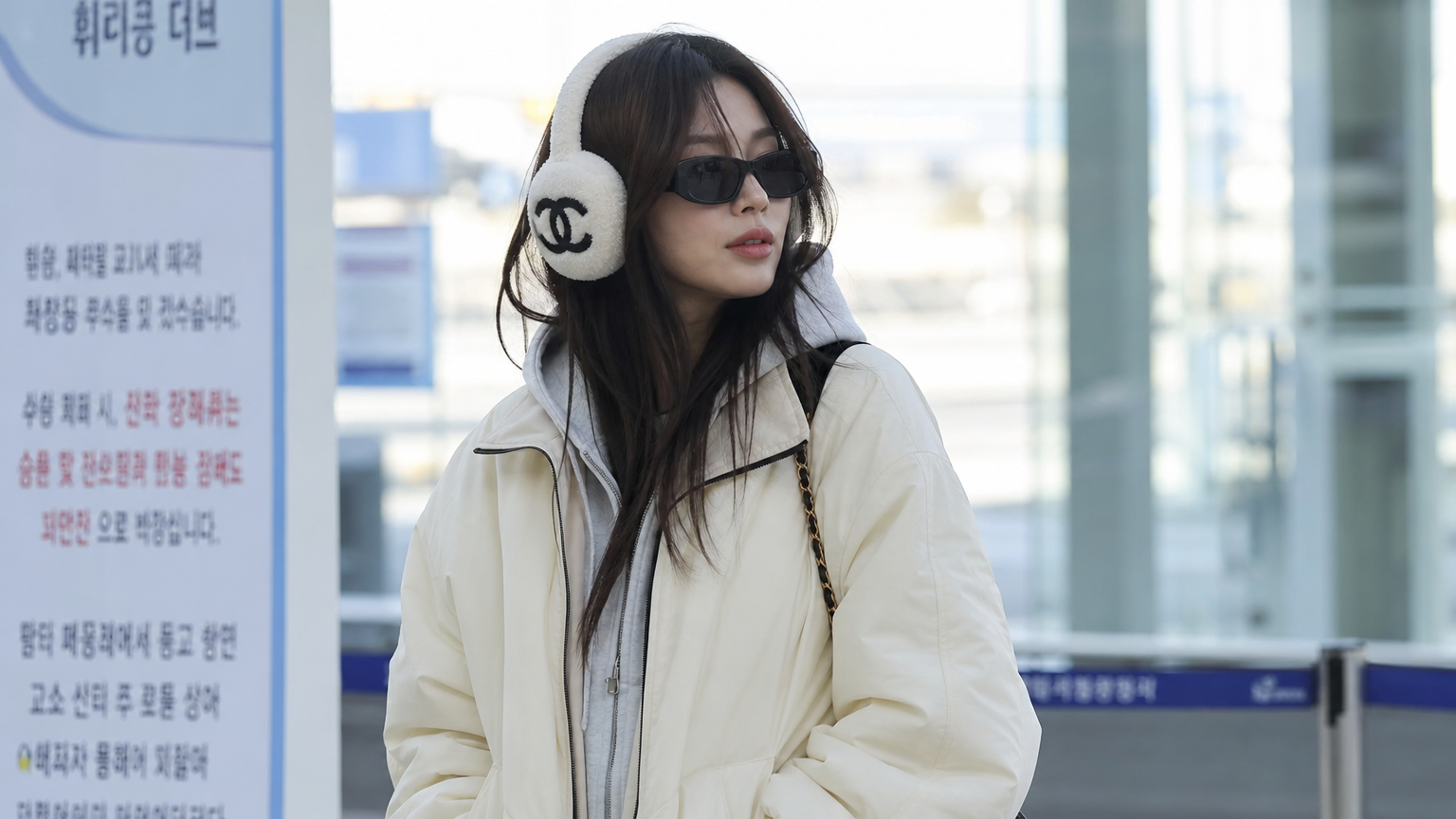 공항 터미널에서 캐주얼 복장과 샤넬 귀마개 및 선글라스를 착용한 인플루언서의 모습