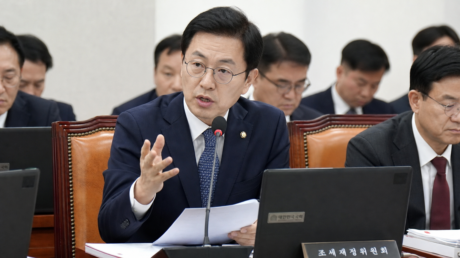 입법 회의에서 동료들과 금융 정책을 논의하는 한국 세무 관료 출신 정치인의 모습
