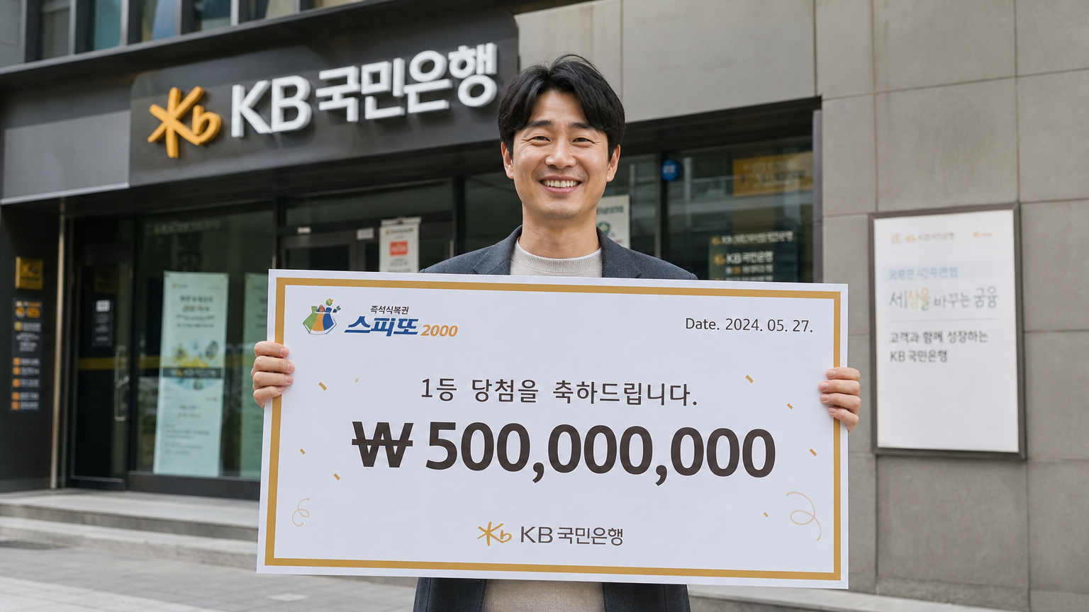 은행 건물 밖에서 큰 복권 수표를 들고 미소 짓는 한국 남성