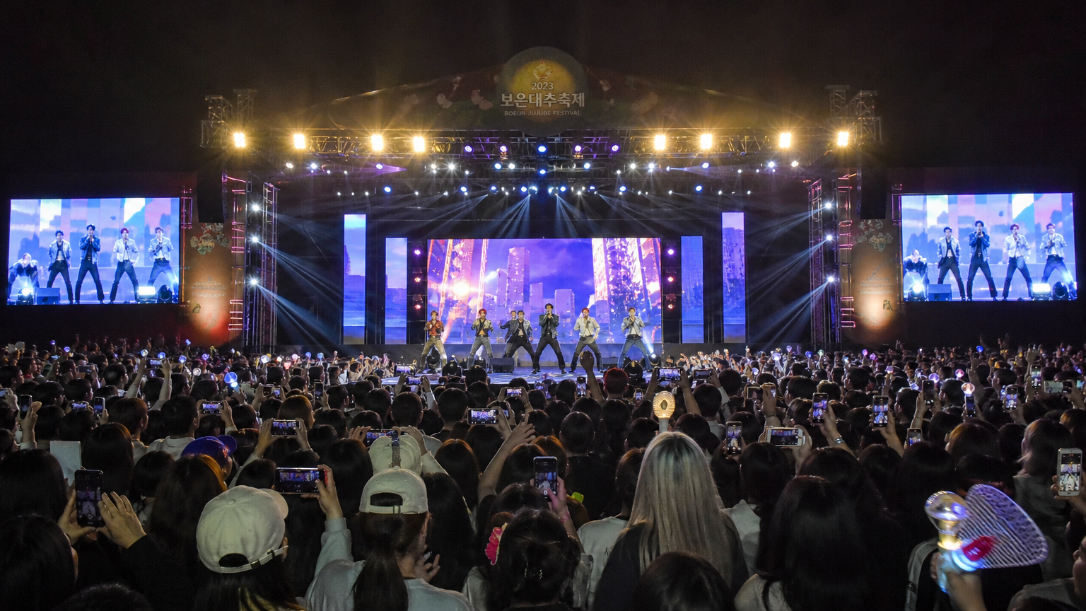 유명 아이돌 그룹이 무대에서 공연하며 관객들이 환호하는 활기찬 콘서트 장면