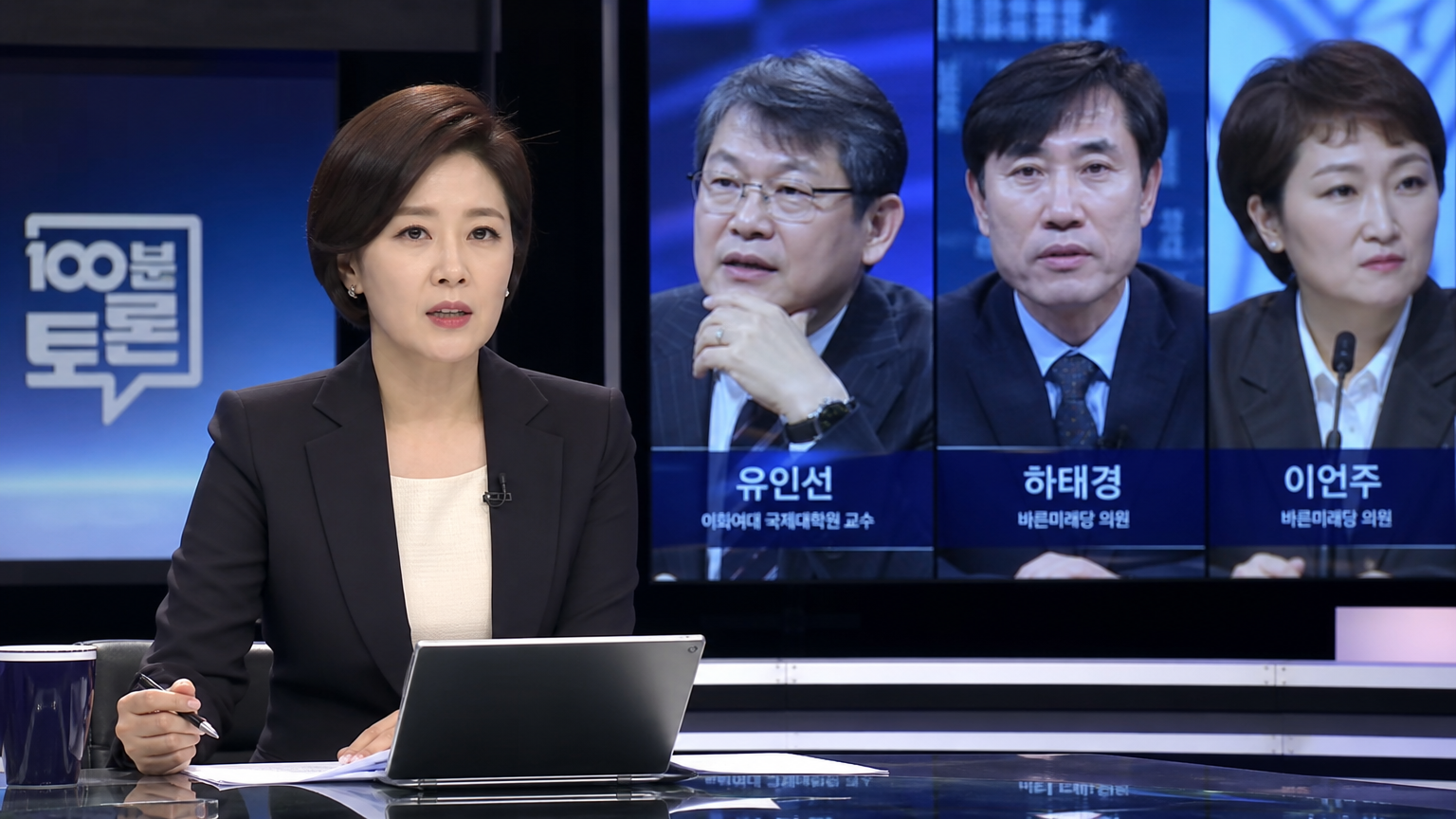 수트를 입고 대형 화면과 첨단 장비가 있는 세트장에서 토크쇼를 진행하는 뉴스 앵커 손석희