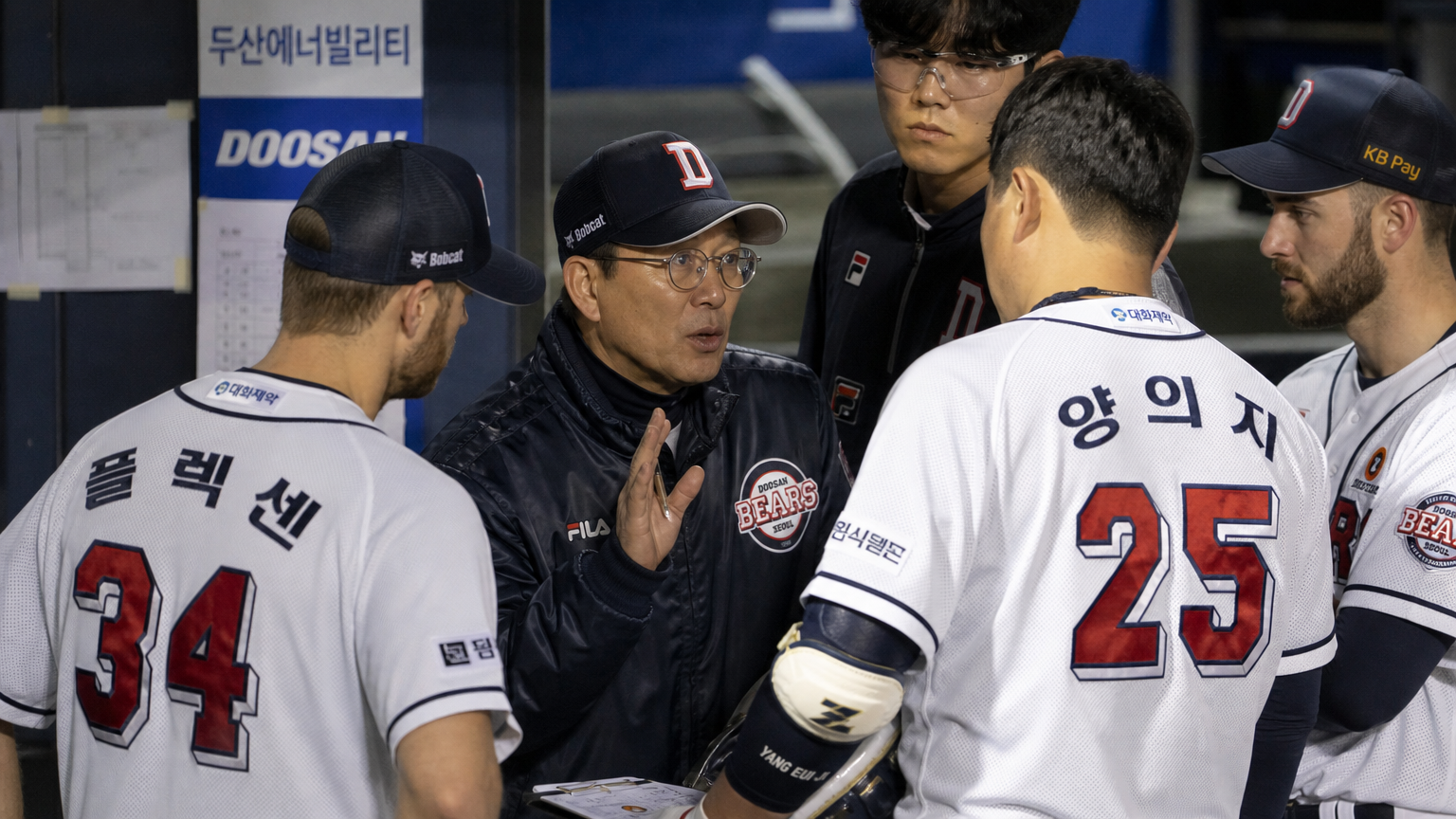 한국 야구 감독이 더그아웃에서 외국인 선수들과 전략 논의 중인 모습