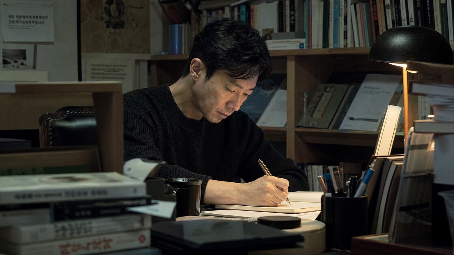 책과 따뜻한 조명이 있는 작업실에서 집중하여 글을 쓰는 작가