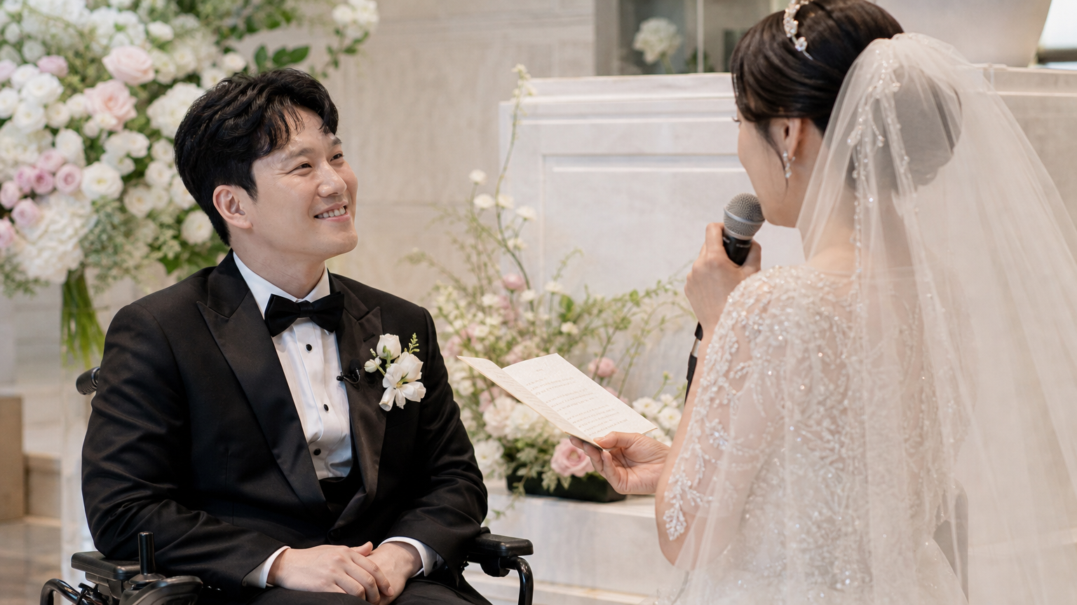 휠체어에 앉은 신랑이 신부에게 미소 지으며 감동적인 서약을 나누는 장면