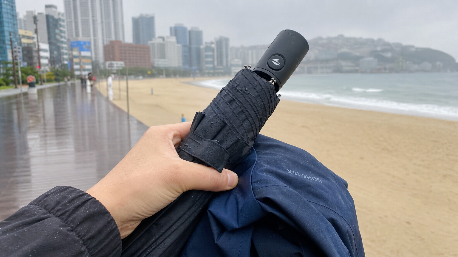 해변 산책로에서 우산과 방수 재킷을 들고 있는 손 클로즈업