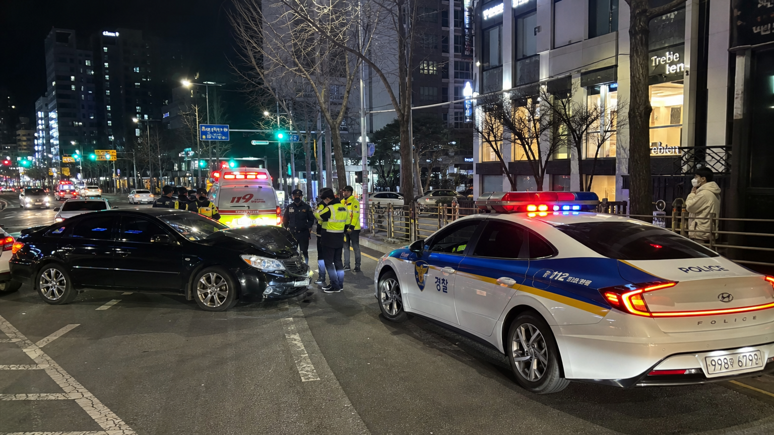 한국 도시의 밤거리에서 작은 교통사고가 발생하여 경찰과 긴급 차량이 출동한 장면