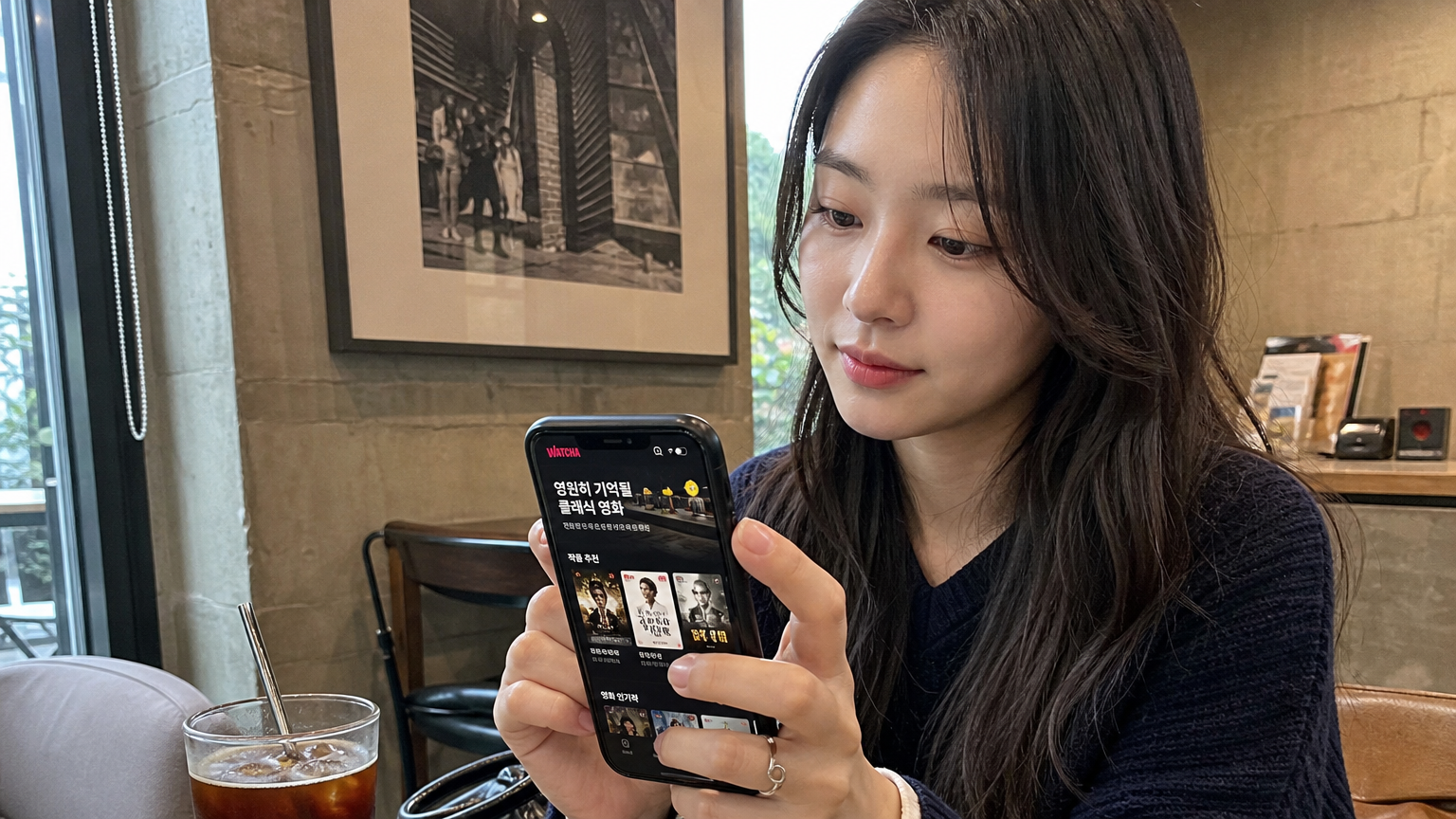 트렌디한 카페에서 스마트폰으로 왓챠 앱을 이용해 클래식 영화 컬렉션을 탐색하는 젊은 여성
