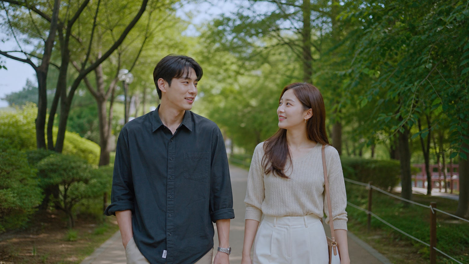 공원에서 천천히 산책하며 대화를 나누는 한국 커플