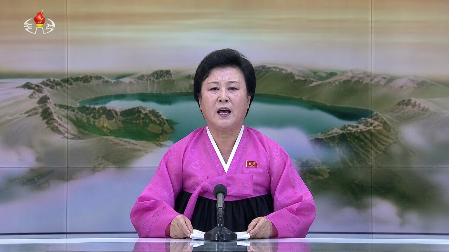 전통적인 스튜디오에서 강렬한 표정으로 긴급 뉴스를 전달하는 상징적인 북한 아나운서