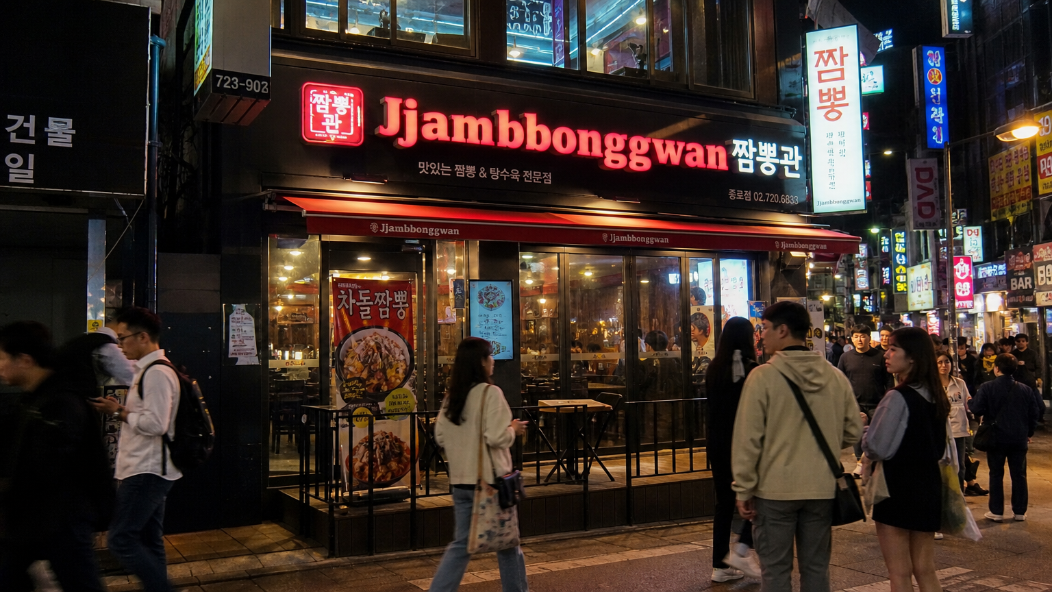 사람들이 지나가는 거리의 '짬뽕관' 네온사인이 빛나는 모습