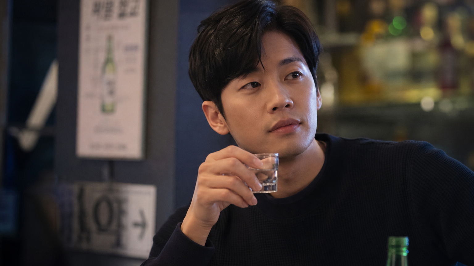 현대적인 바에서 소주잔을 들고 있는 한국 성인의 사려 깊은 표정