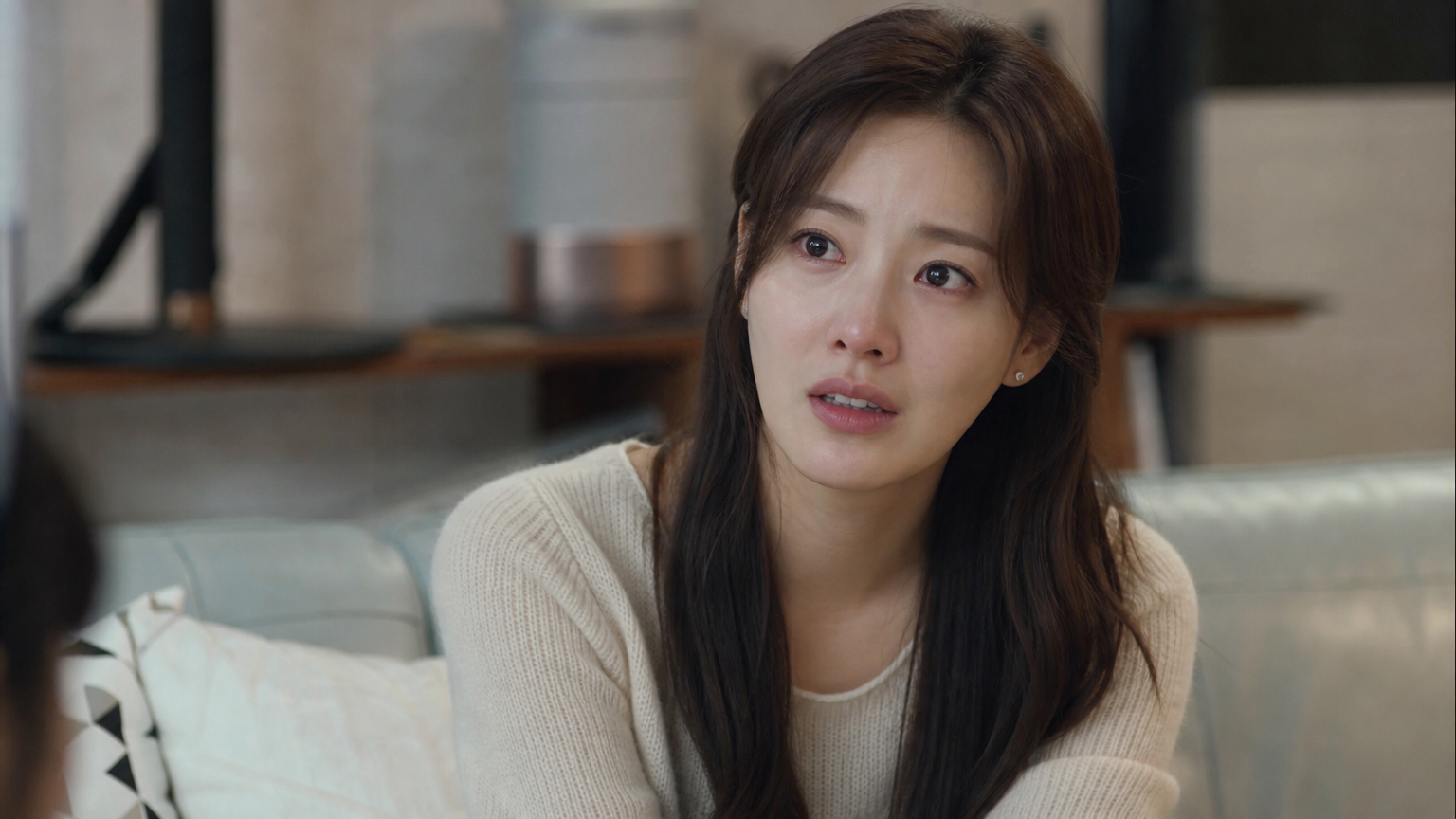 드라마 촬영 중 편안한 거실 세트장에서 미묘한 표정으로 깊은 감정을 표현하는 한국 여배우