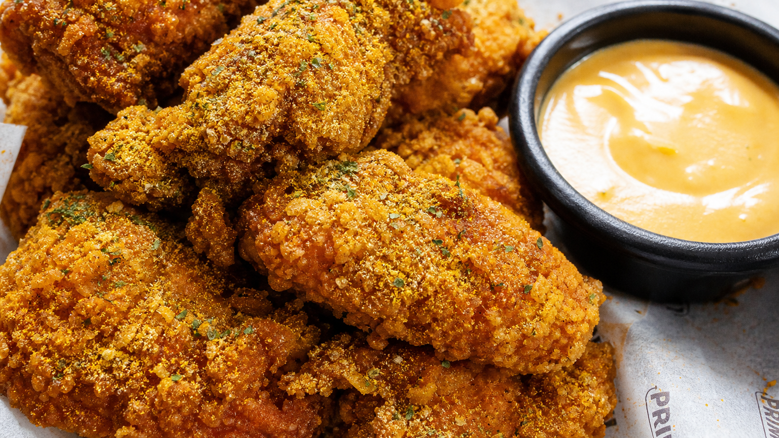 바삭한 황금빛 껍질 위에 특별한 치즈 시즈닝이 뿌려진 뿌링클 치킨과 소스가 담긴 그릇