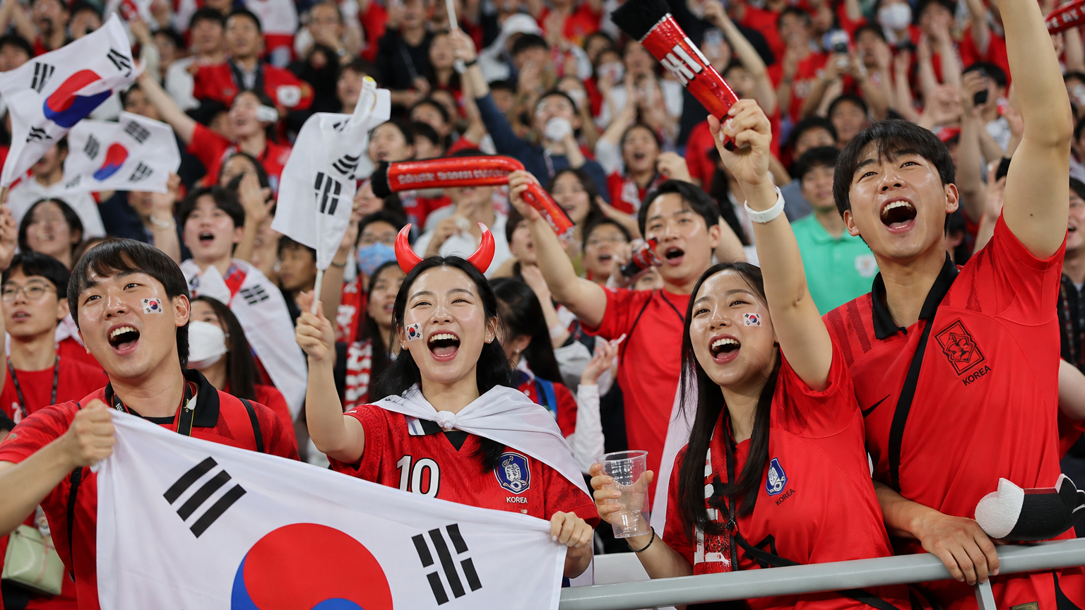 축구 경기장에서 한국 축구 팬들이 열광적으로 응원하는 모습