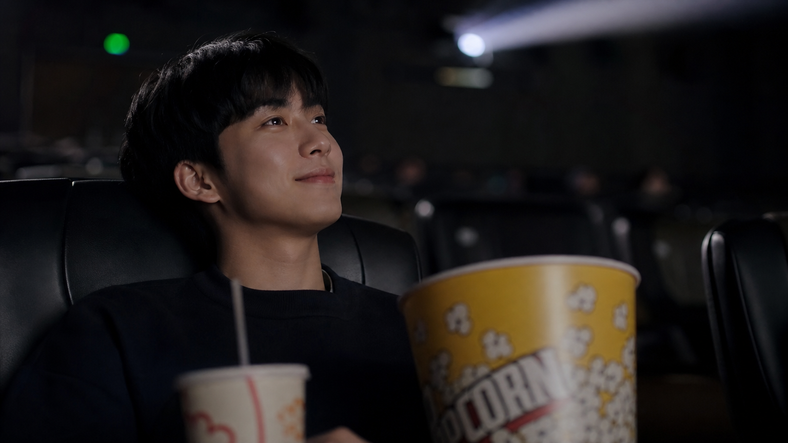 젊은 남성이 팝콘과 탄산음료를 들고 혼자 영화관에서 영화를 보는 모습