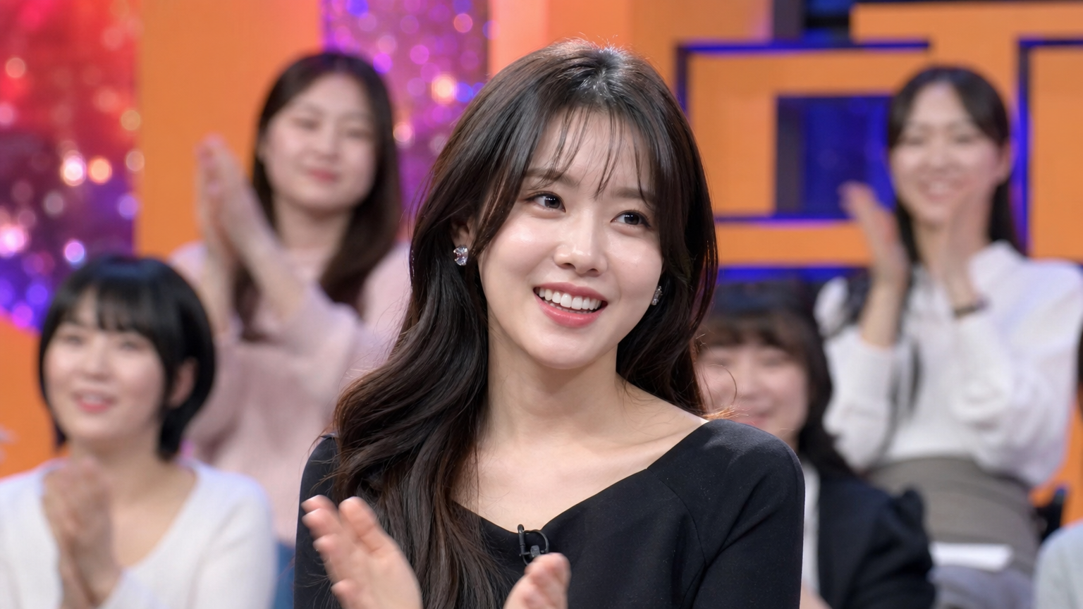 예능 프로그램 세트장에서 청중의 박수를 받으며 활기차게 웃고 있는 한국 여성