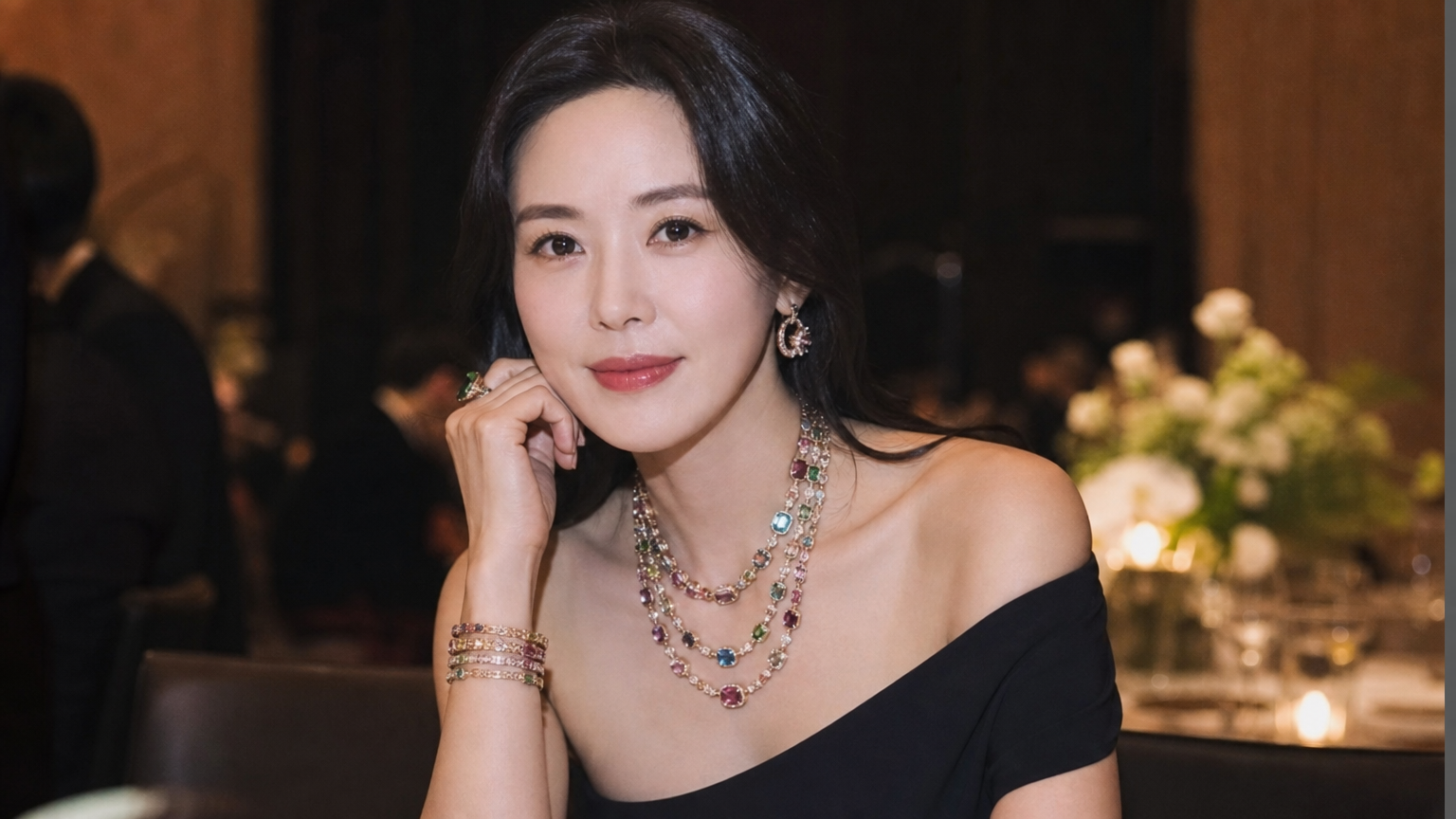 오프숄더 드레스를 입고 다채로운 스톤 주얼리를 레이어드한 여성이 우아한 행사에 참석한 모습