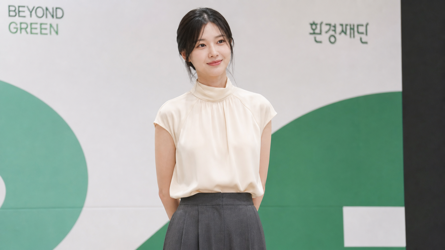 아이보리색 하이넥 반소매 블라우스를 회색 와이드 팬츠와 함께 공식 행사장에서 착용한 모습