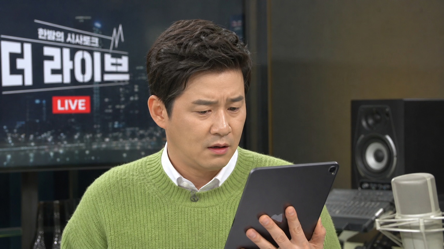 한국 TV 진행자가 스튜디오에서 태블릿으로 SNS 댓글을 읽고 있는 모습