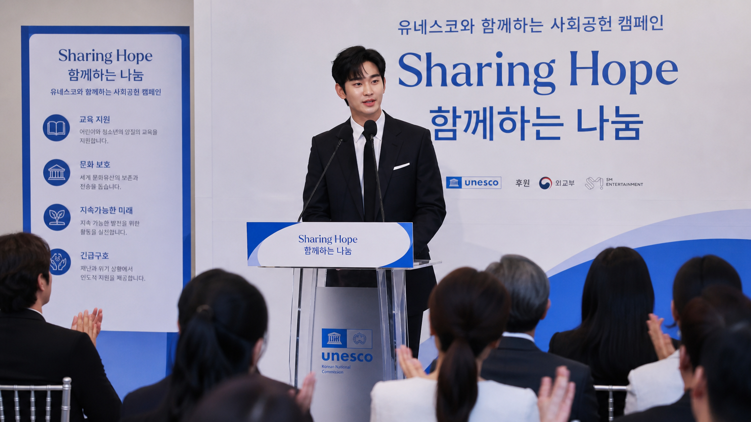 잘 차려입은 한국 연예인이 자선 행사 무대에서 연설하는 모습