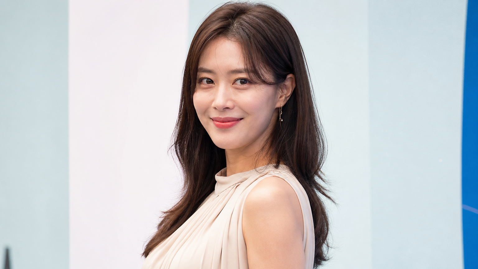 30대 초반의 여배우가 밝은 세트장에서 자신감 있는 포즈를 취하는 모습