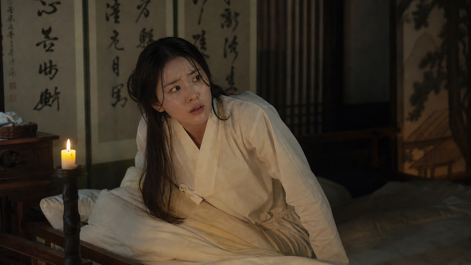 조선 시대 방에서 깨어난 여성의 당황한 표정과 촛불이 어우러진 장면