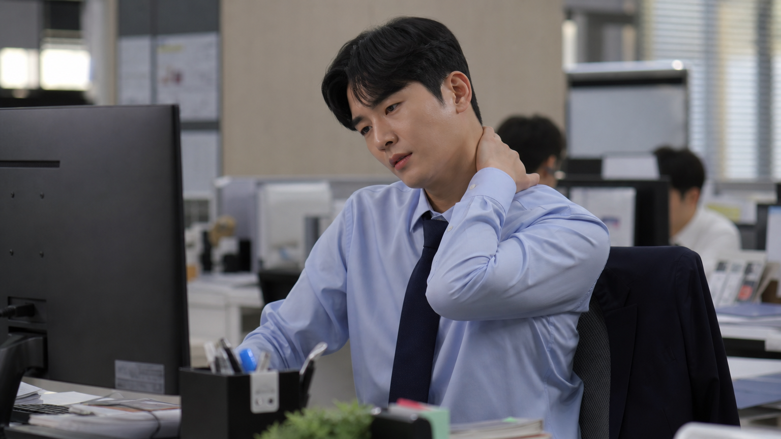 사무실 책상에 앉아 컴퓨터 화면을 보며 목을 주무르는 직장인