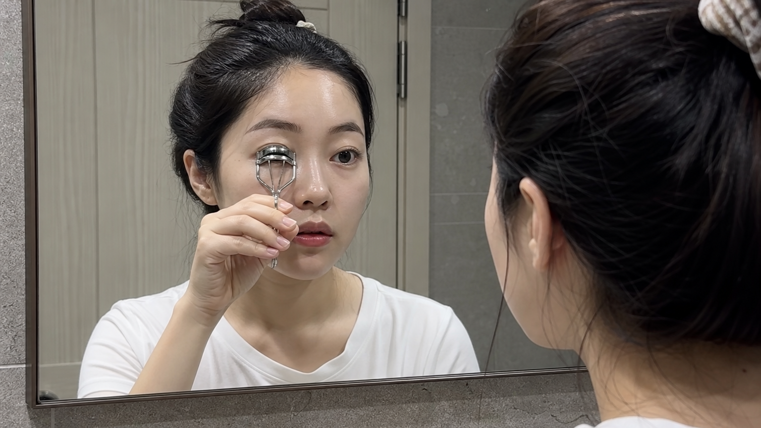 욕실 거울 앞에서 집중하여 속눈썹 컬러를 사용하는 여성
