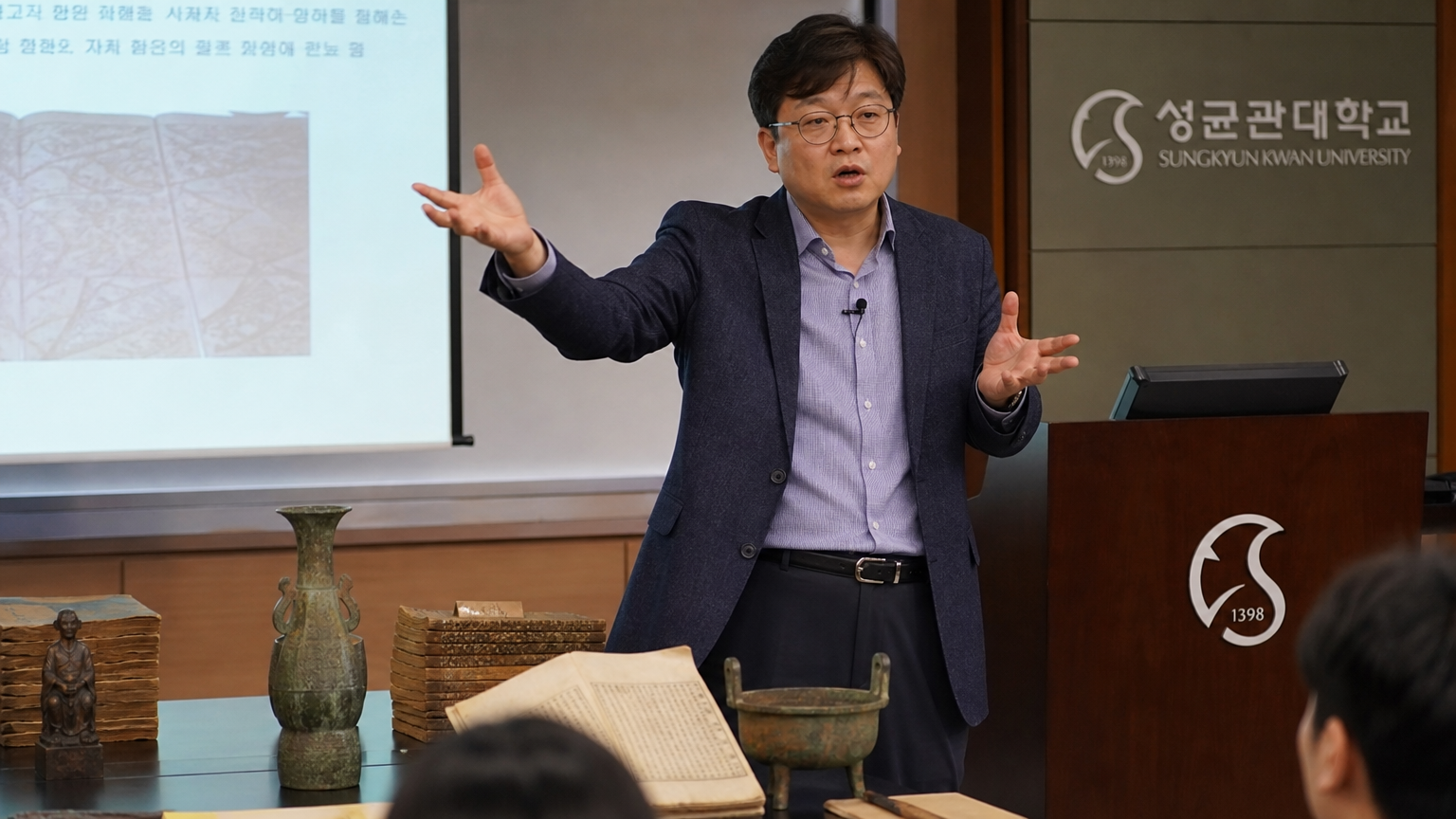 한국사 교수가 성균관대에서 역사 유물을 배경으로 강의를 하는 모습