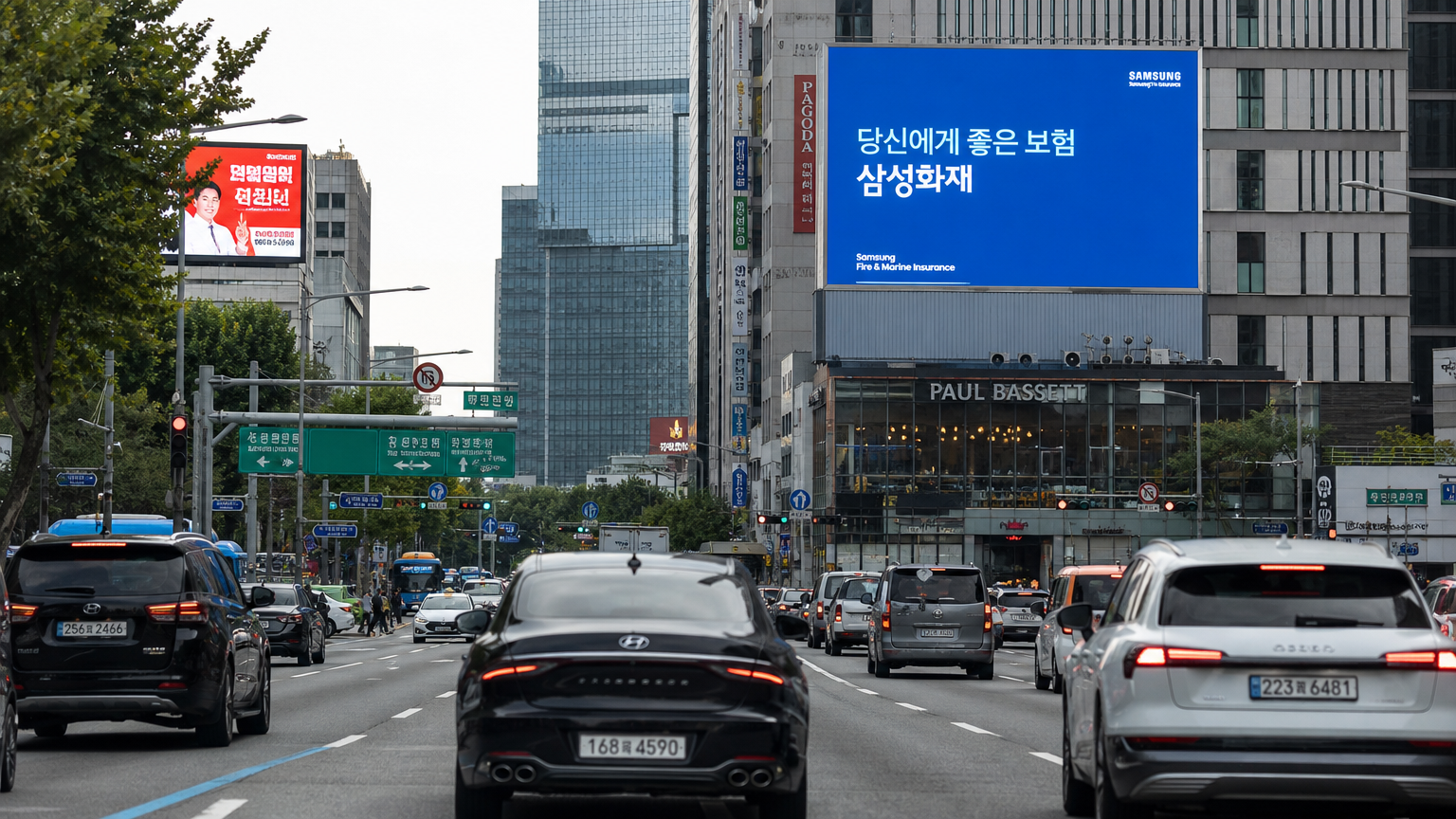 바쁜 한국 도시의 도로에서 다양한 차량과 보험 광고가 보이는 모습