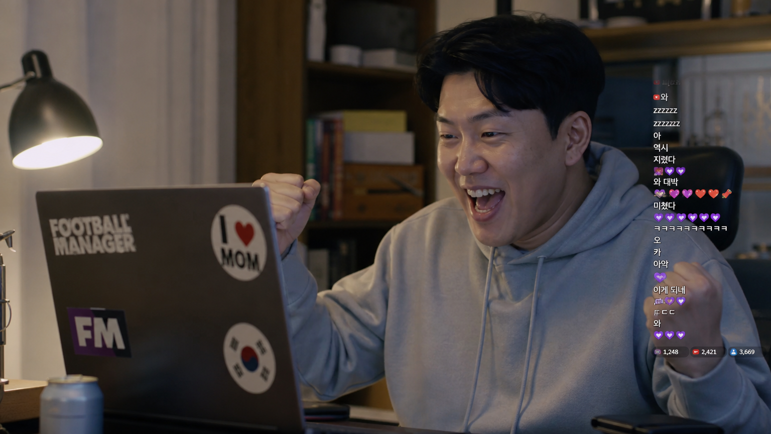 한 남성이 방 안에서 노트북으로 축구 매니저 게임 방송을 시청하며 즐거워하는 모습
