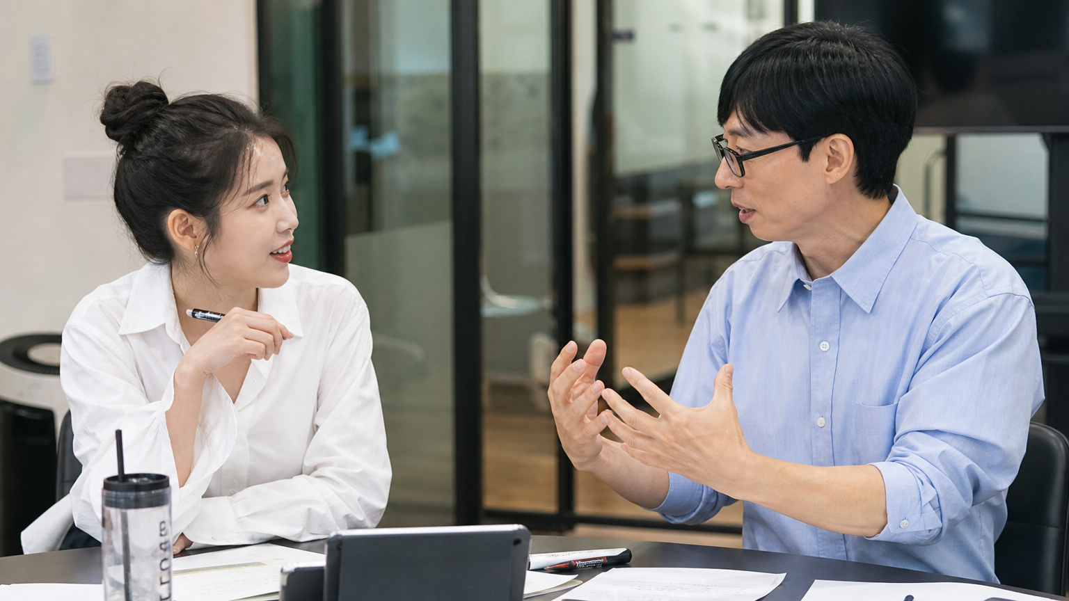 현대적인 사무실에서 함께 아이디어를 나누는 아이유와 유재석