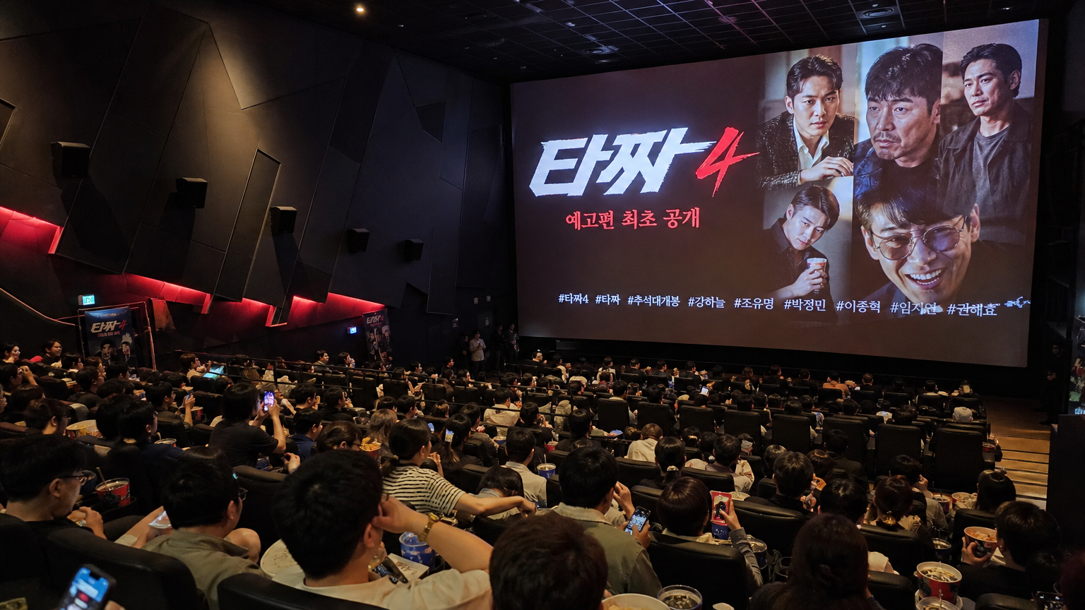 현대적인 한국 영화관에서 타짜4 예고편을 기다리며 팝콘과 음료를 들고 있는 팬들의 활기찬 모습