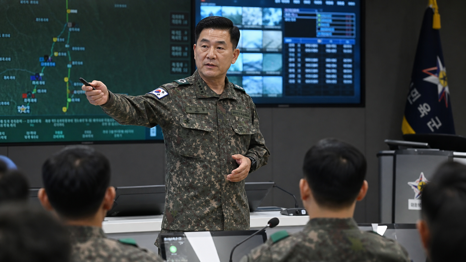 전략 지도가 놓여진 현대식 회의실에서 군복을 입고 병사들에게 연설하는 중년 장교의 모습