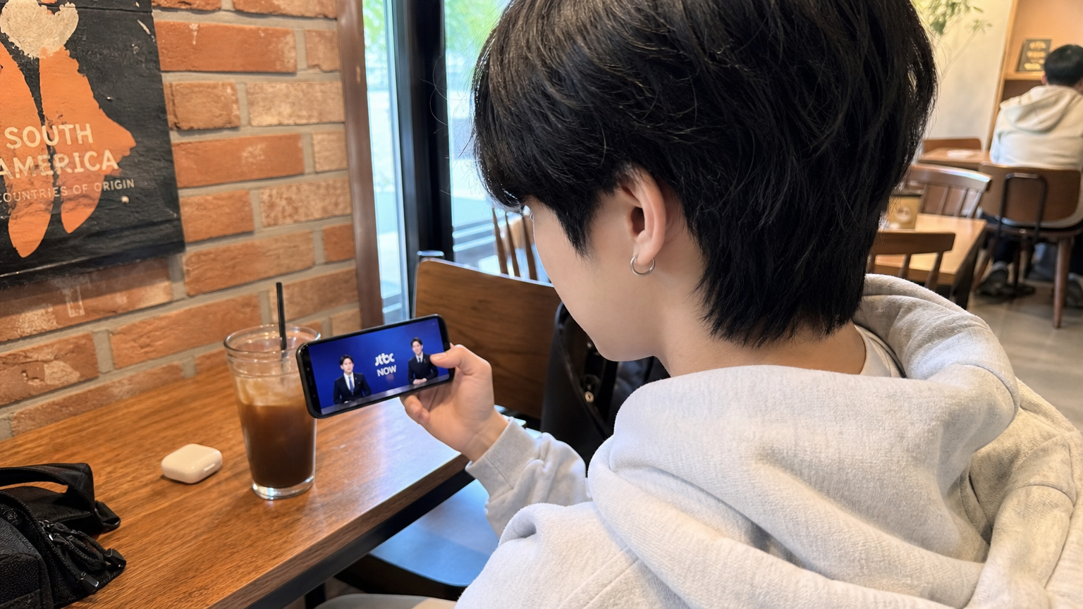 최신 유행 카페에서 스마트폰으로 'JTBC NOW' 앱을 통해 라이브 방송을 시청하는 젊은 사람의 모습