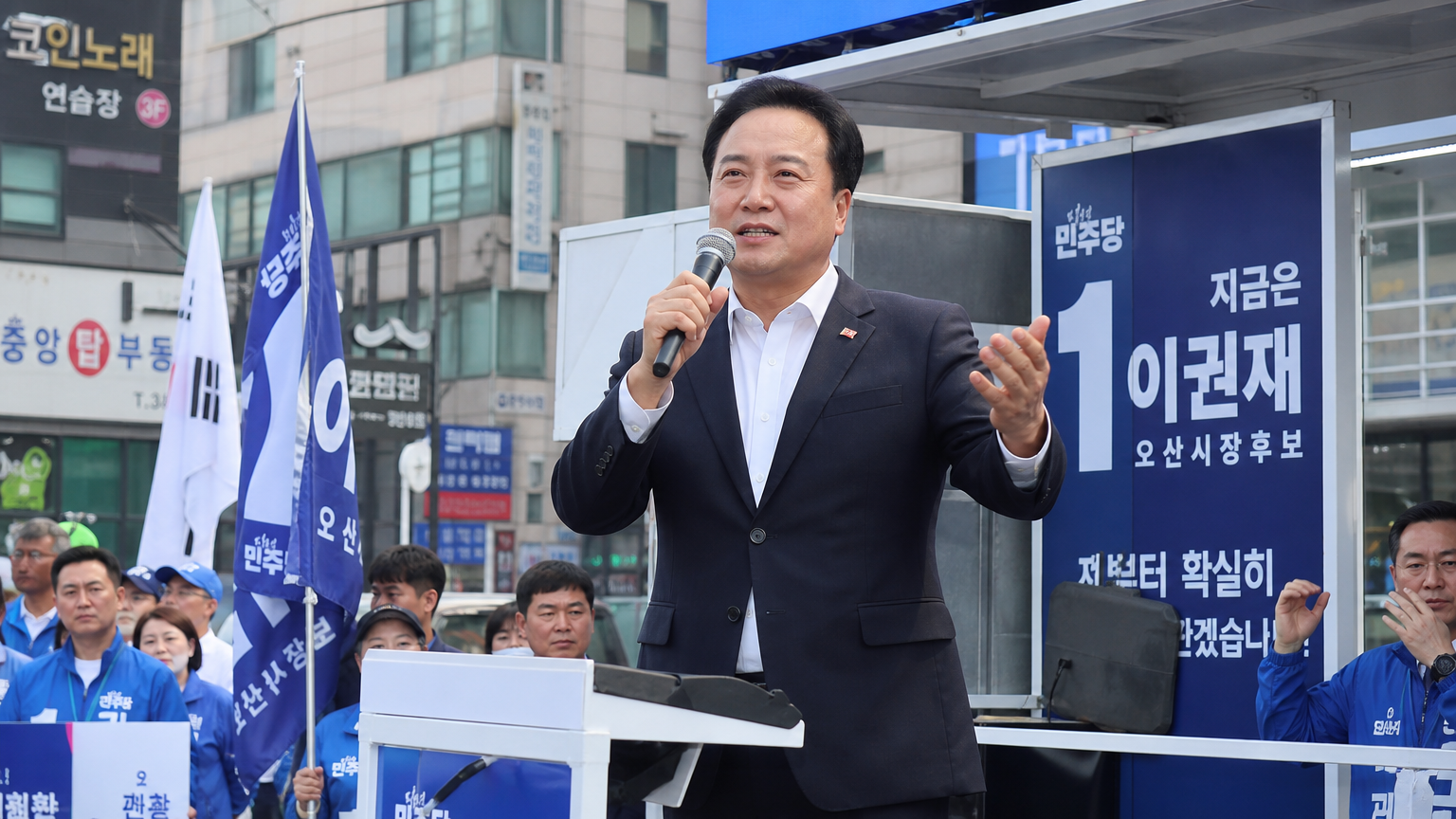현대적인 오산 도시 배경에서 지지자들과 연설하는 정치인의 모습