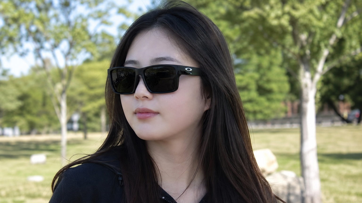 둥근 얼굴형의 젊은 여성이 공원에서 스퀘어 프레임의 오클리 선글라스를 써보는 장면