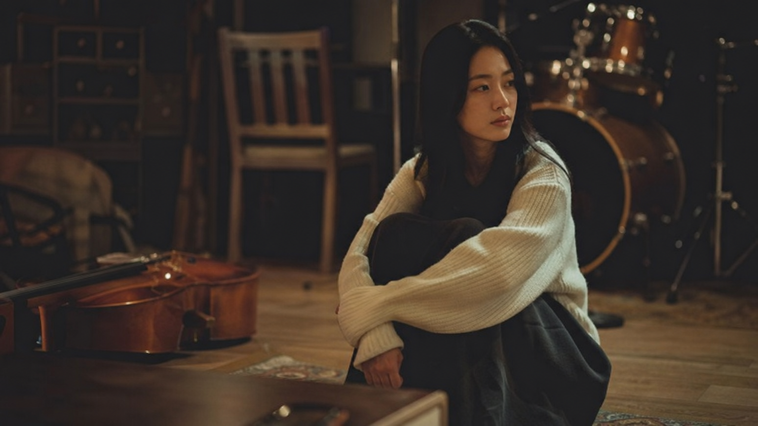 어두운 방에서 버려진 악기들 사이에 앉아있는 한국 여성
